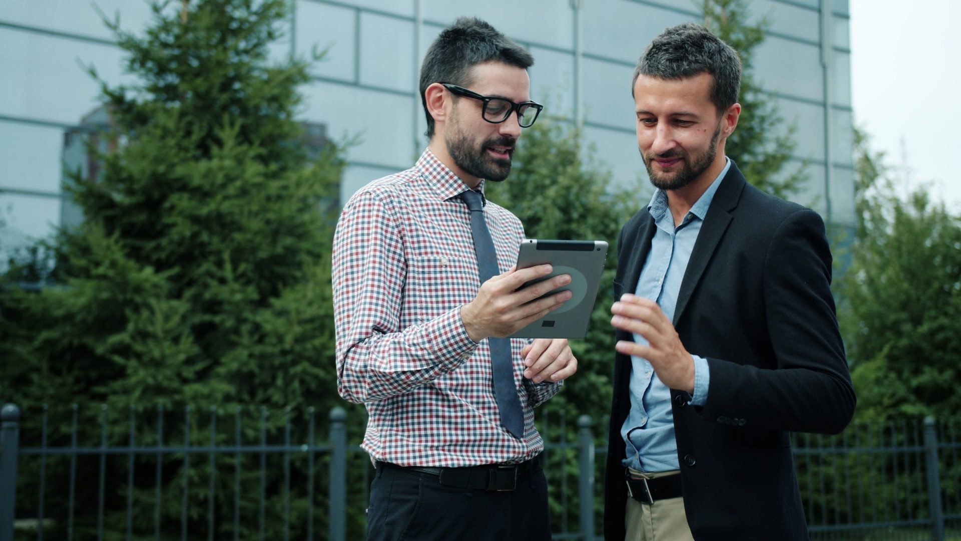 Two businessmen discussing work on a tablet in an outdoor setting.
