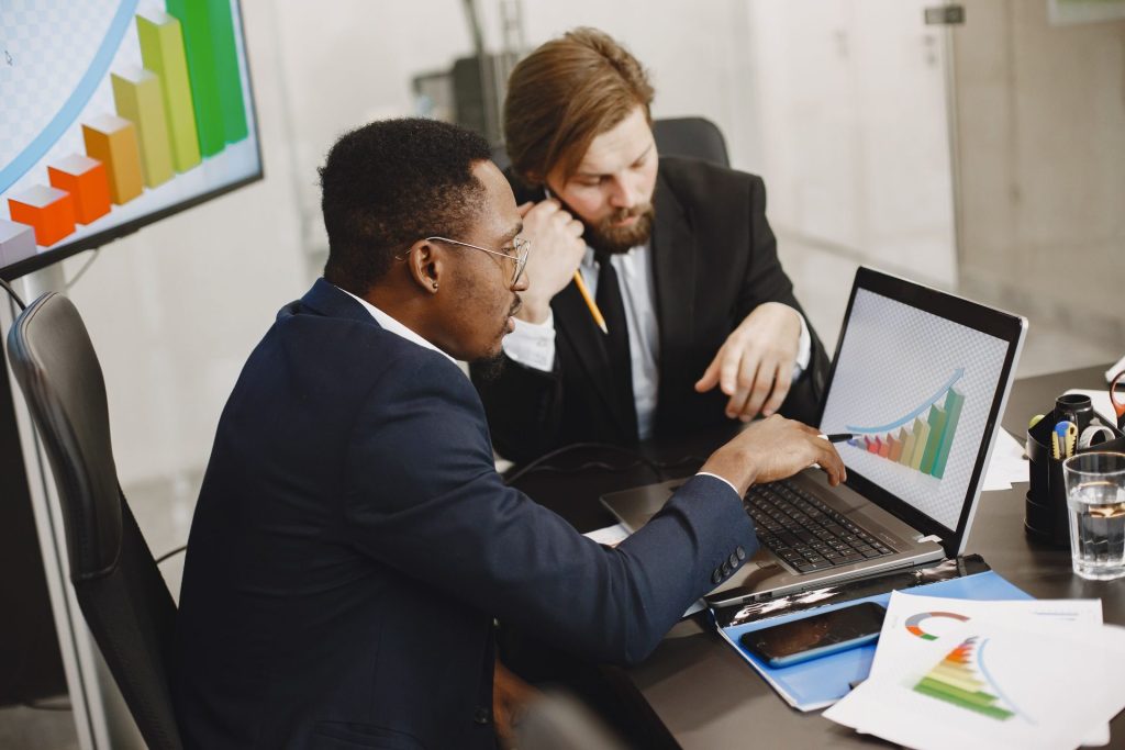 Two business professionals working on growth charts using laptop in an office setting.